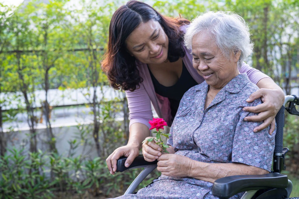 asian carer looking over older lady in a wheelchair
