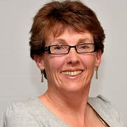 Photograph of Kaye facing the camera, short hair, glasses and earrings