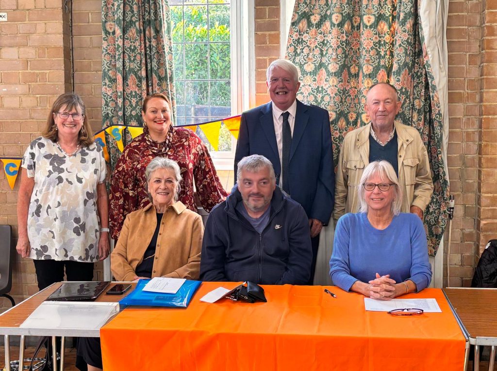 3 people sitting behind a table and 4 standing behind them